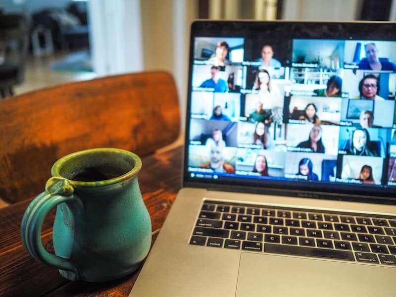 Laptop displaying a zoom call sits on a desk next to a mug.