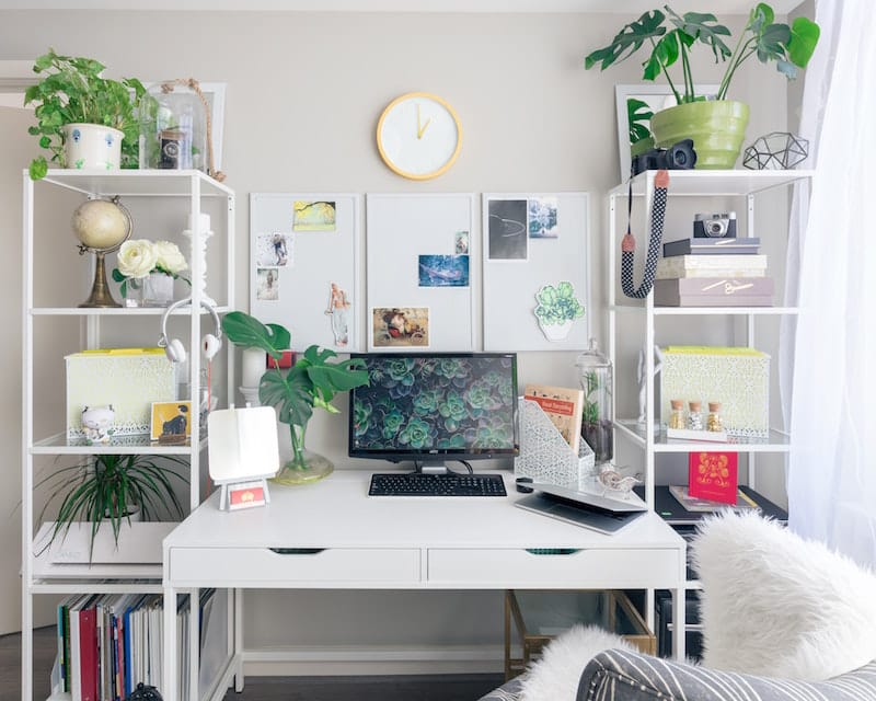 A white desk is bathed in sunlight, decorated with green plants and fun personal items to help you stay positive.