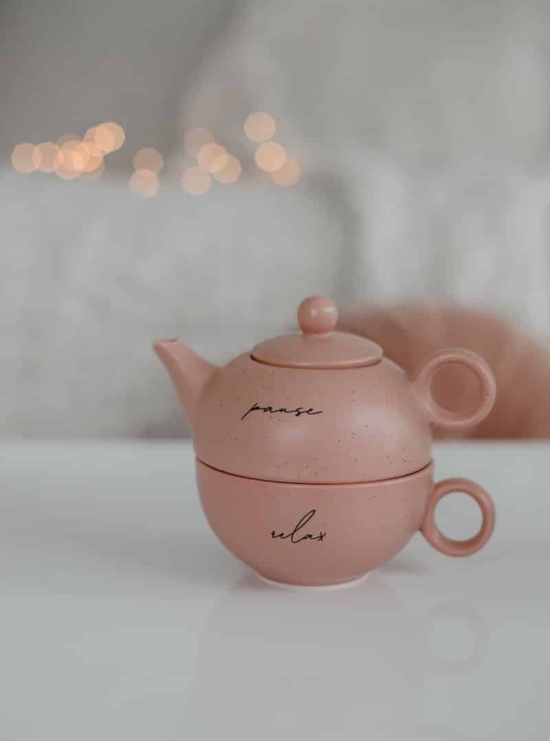 A pink teapot with the words, "pause" and "relax" sits on a table