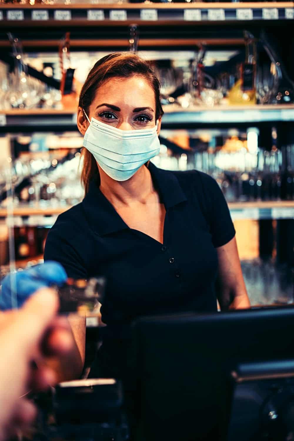 A cashier wearing a mask hands a customer their credit card